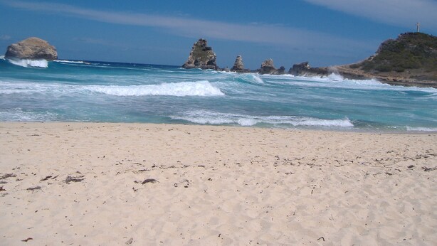 A beach with clear blue water, sandy shore, and rocky outcrops.