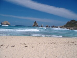 Uma praia com águas azul-claras, areal arenoso e afloramentos rochosos.