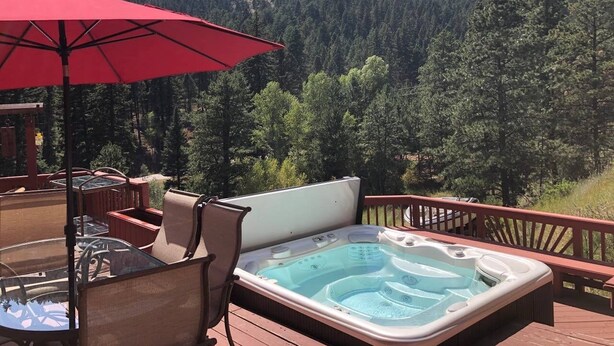 Un bain à remous sur une terrasse, agrémenté d’un parasol rouge, avec en arrière-plan une montagne boisée.
