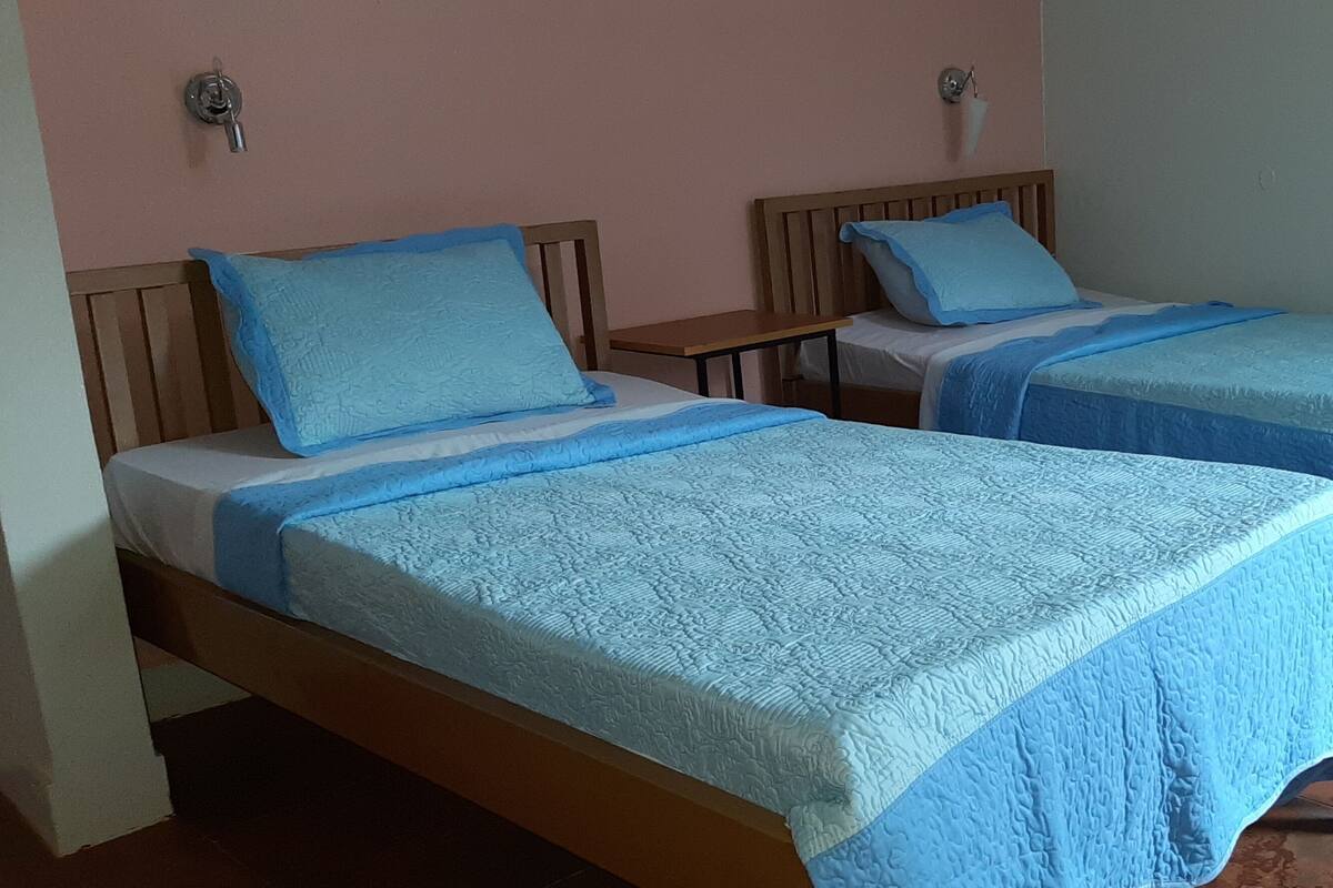 Duas camas de solteiro com cabeceiras de madeira, uma mesa pequena e uma fechadura na parede.