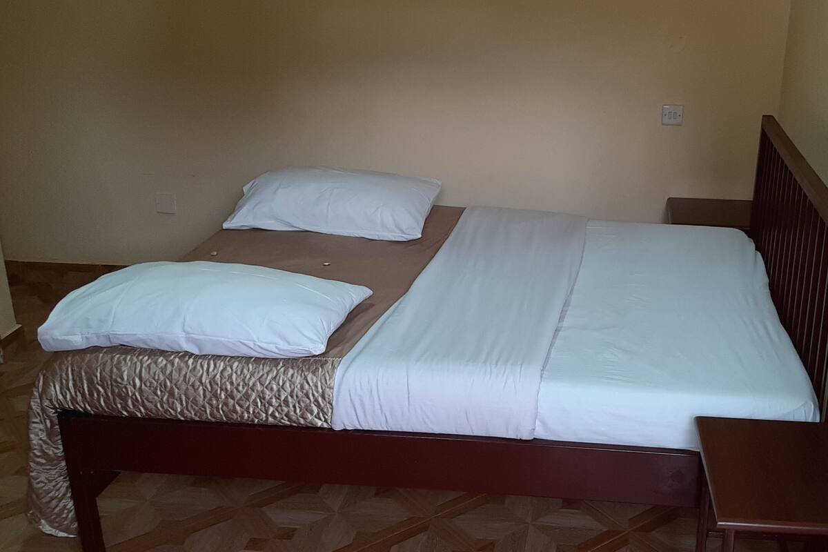 Uma cama de solteiro com estrutura de madeira, cabeceira e duas almofadas.