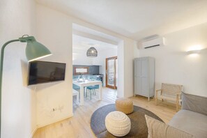A modern living room with a flat-screen TV, a green desk lamp, a grey sofa, and a round rug.