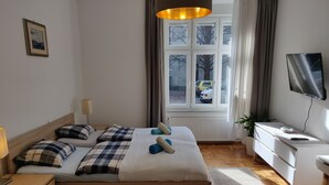 Une chambre à coucher avec un lit, des tables de chevet, un bureau, une télévision et une fenêtre avec des rideaux.