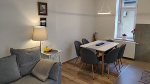 Un salon moderne avec un canapé gris, une table à manger avec des chaises, une lampe et une fenêtre donnant sur un beau paysage.