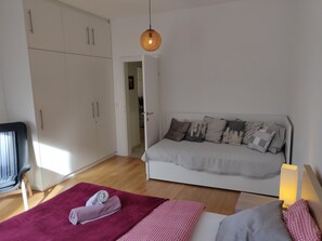 A bedroom with a white wardrobe, a grey sofa with patterned cushions, a red blanket, and a checkered bedspread. - Luxury Spa Apartment (Zagreb)