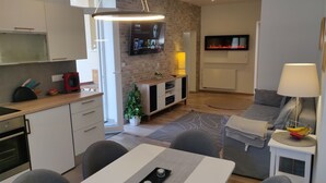 Une cuisine moderne avec un coin repas, un canapé gris et un téléviseur fixé au mur.