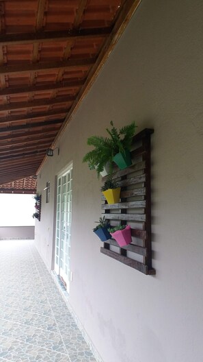 A covered outdoor area with a tiled floor, a wooden ceiling, and a wall-mounted plant shelf with various potted plants.