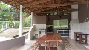 An outdoor kitchen area with a wooden table and chairs, a sink, and a stove. - Chacara Recanto Paraíso is in a privileged location. (Serra Negra)