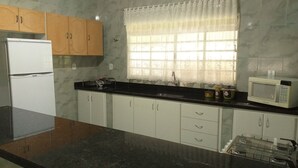 A kitchen with white cabinets, a black countertop, a white refrigerator, a microwave, and a window with lace curtains. - Chacara Recanto Paraíso is in a privileged location. (Serra Negra)