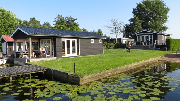 Een pand aan het meer met een aanlegsteiger, een gazon en een klein gebouw met grote ramen.