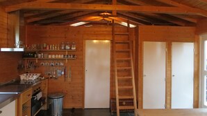 Een houten chalet van binnen met een keukenhoek, een houten trap en een deur.