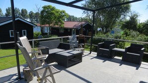Een terras buiten met rieten meubels, waaronder stoelen en een bank, op een betegelde vloer.