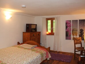 A bedroom with a wooden bed, a wooden dresser, a chair, a window with curtains, and a wall with framed pictures.