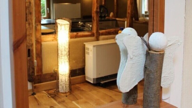 Un intérieur avec une structure en bois, comprenant un coin cuisine, une lampe allumée et une étagère ornée d’objets décoratifs.