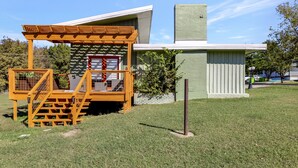 Un bâtiment moderne doté d’une pergola en bois et d’un petit espace clos avec une porte rouge.