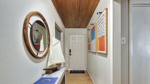 Un couloir avec un plafond en bois, une porte blanche et un banc sur lequel sont posés une maquette de voilier et un classeur bleu.