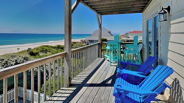 A wooden deck with a view of the beach, outdoor seating, and a house with a balcony. - Tipsy Turtle | Ocean Views + Pool! (North Topsail Beach)