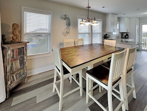 A dining area with a wooden table and white chairs, a kitchen with white cabinets, and a decorative wall piece.