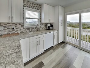 A modern kitchen with white cabinets, a granite countertop, a built-in sink, and a coffee maker. - Tipsy Turtle | Ocean Views + Pool! (North Topsail Beach)