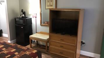 Quarto com cama, cômoda de madeira com televisão, pequena escrivaninha e geladeira.