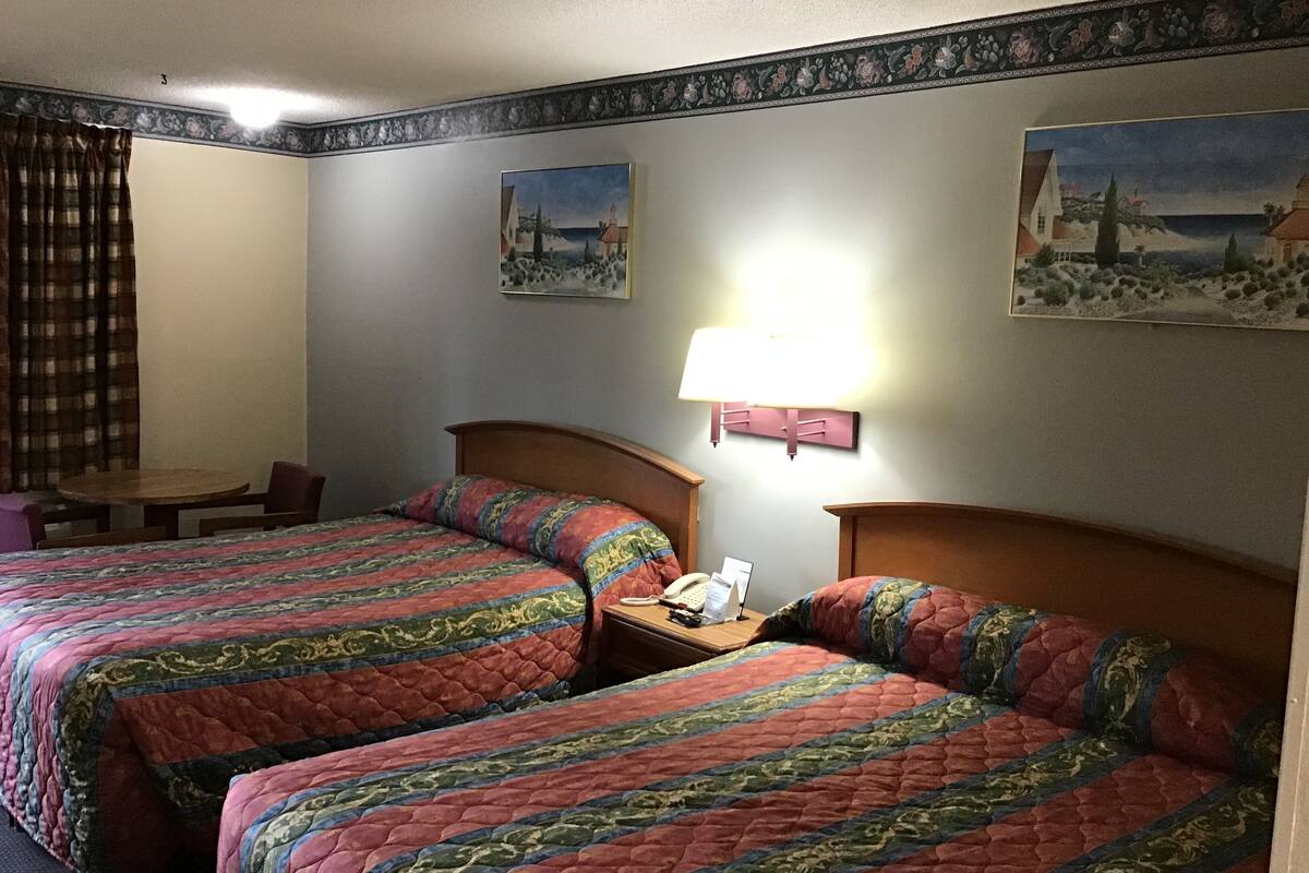 Habitación de hotel con dos camas, una mesita, una lámpara y dos cuadros en la pared.