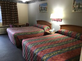 Habitación de hotel con dos camas, un escritorio, una silla y una lámpara.