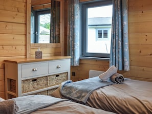 A bedroom with a wooden headboard, a bedside table with a mirror, a window with curtains, and a bed with a blanket.