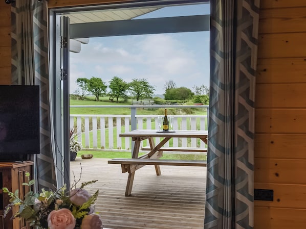 An open doorway leading to a wooden deck with a table and chairs, a bottle of champagne, and a television on a stand.