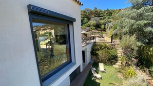 A modern building with a large window overlooking a landscaped garden and hillside. - house wtih swimming pool and large garden. Sea view (Bormes-Les-Mimosas)