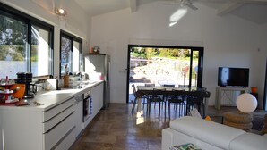 A modern kitchen with a dining area, a TV, and a balcony with a view of the outdoors. - house wtih swimming pool and large garden. Sea view (Bormes-Les-Mimosas)