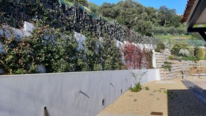 A modern building with a white exterior wall, a stone retaining wall, and a landscaped garden area with gravel and small plants. - house wtih swimming pool and large garden. Sea view (Bormes-Les-Mimosas)