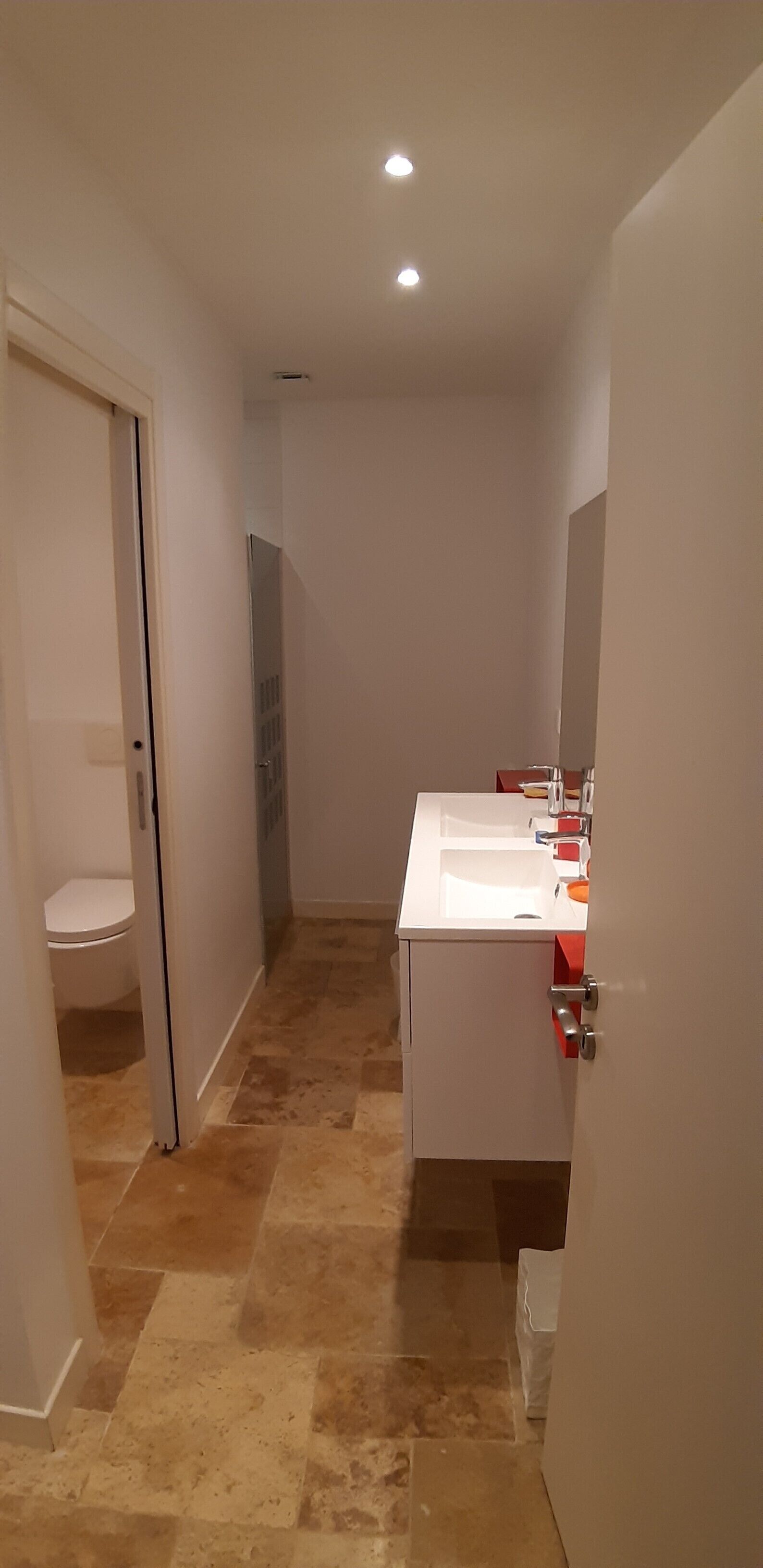 Un baño estrecho con un lavamanos blanco, un espejo y un inodoro visible al fondo.
