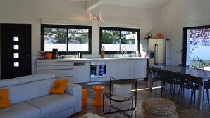 A modern kitchen with white cabinets, a dining area with a table and chairs, and a sofa with orange cushions. - house wtih swimming pool and large garden. Sea view (Bormes-Les-Mimosas)