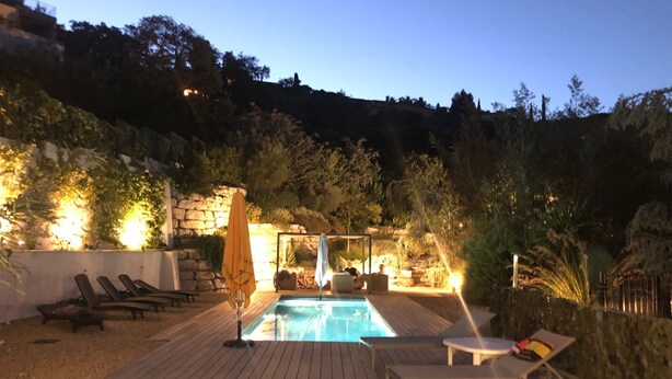 A pool area with lounge chairs and a table, surrounded by a wooden deck and stone walls. - house wtih swimming pool and large garden. Sea view (Bormes-Les-Mimosas)