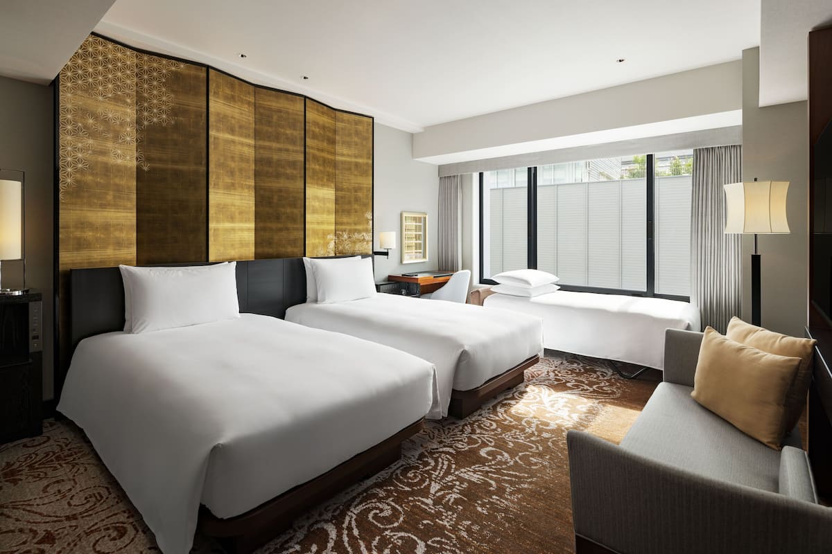 A hotel room with two beds, a sofa, a large window, and a decorative wall panel.