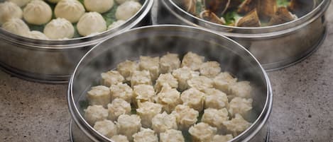 Three metal steamer baskets with food, one containing dumplings, another with a different type of dumpling, and the third with what appears to be meat and vegetables.