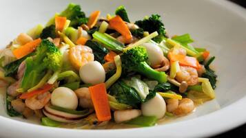 Une assiette blanche contenant un plat de légumes sautés, avec des crevettes, des brocolis, des carottes et d’autres légumes.
