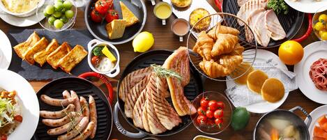 Diversos alimentos, como carnes a la parrilla, salchichas y pasteles, sobre una mesa de madera.