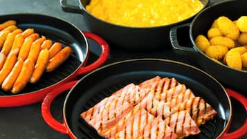 Una parrilla con salchichas, salmón a la parrilla y mazorcas de maíz.