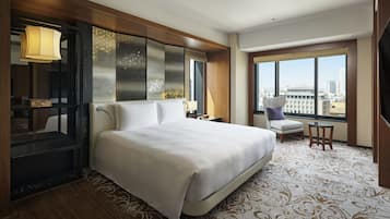 Ett hotellrum med en stor säng, ett skrivbord, en stol, en TV och utsikt över staden.