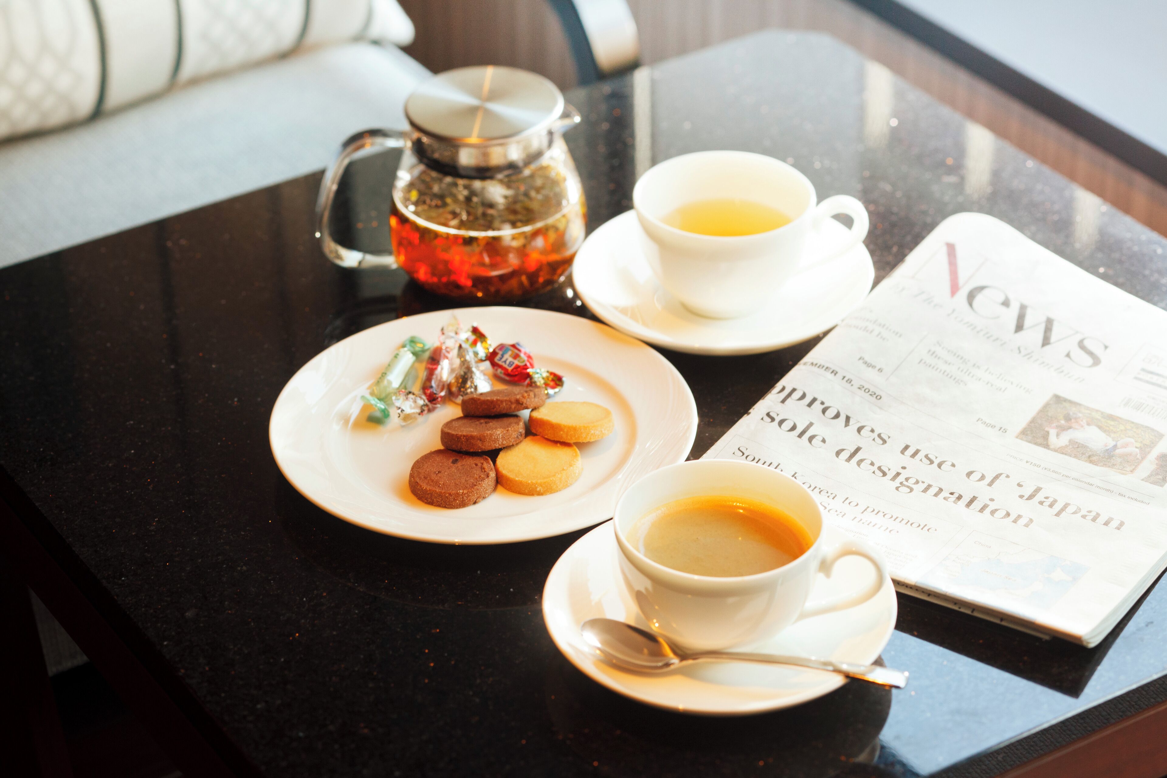Une table avec un journal, une tasse de thé, une assiette de biscuits et une théière.