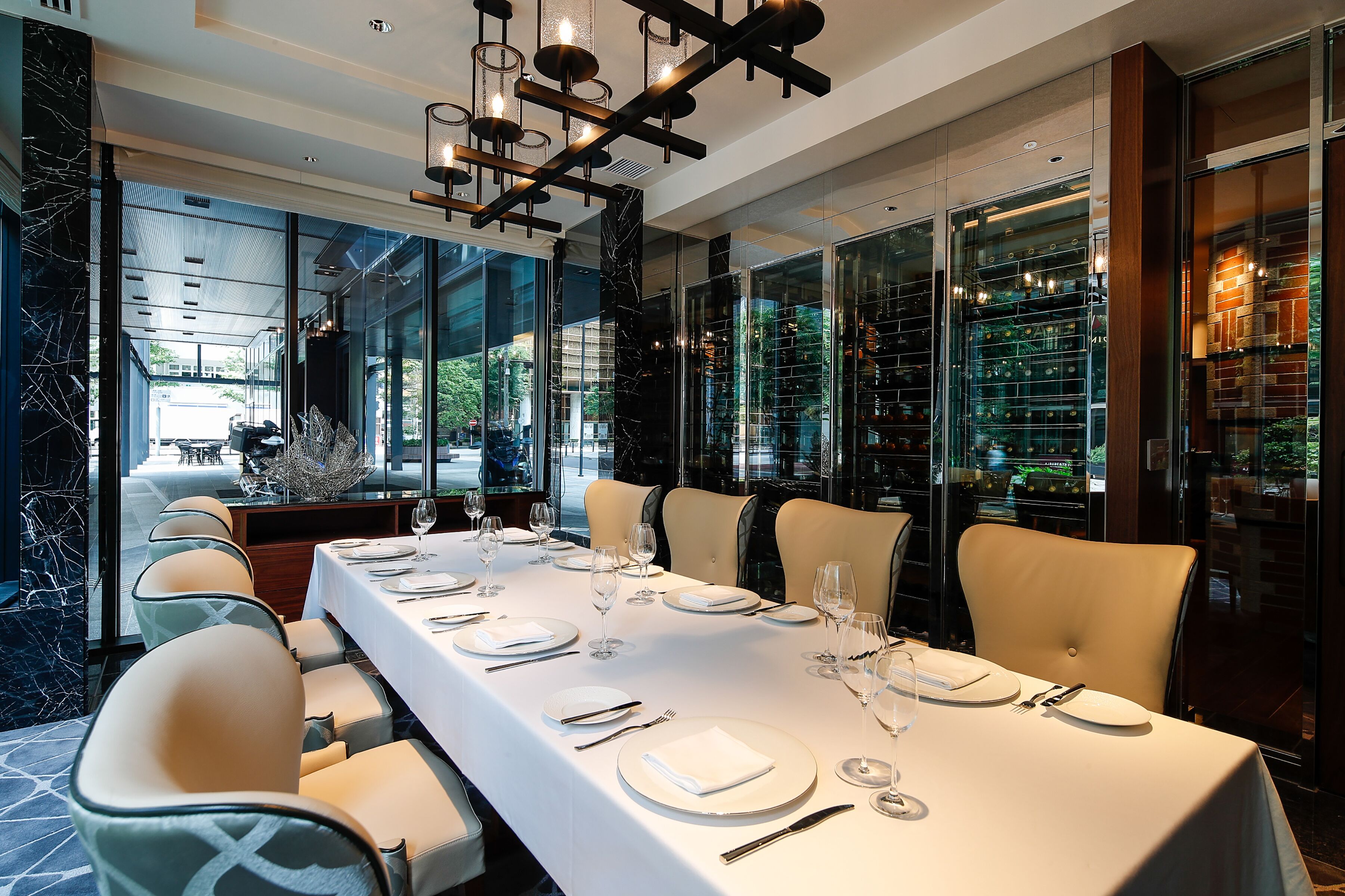 A dining area with a long table set for six, modern chairs, and a chandelier.