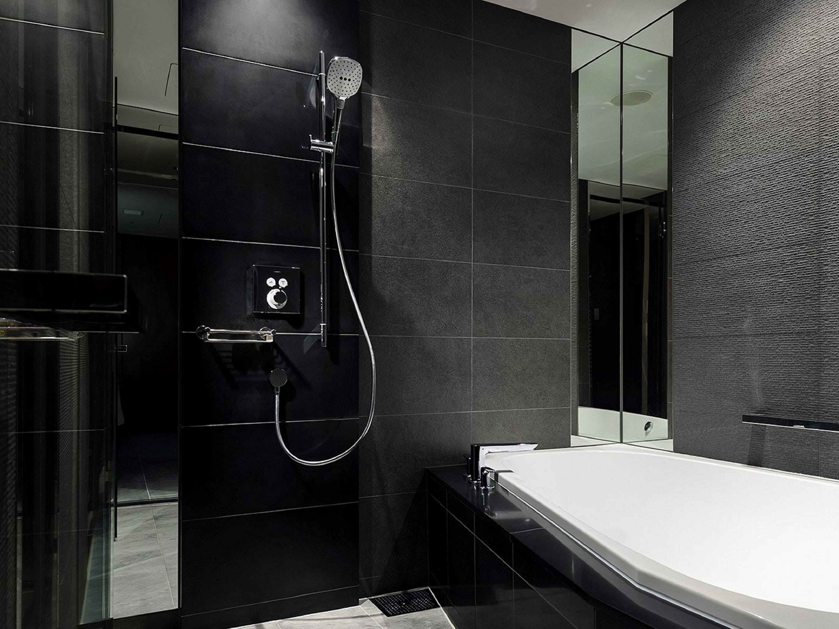 Un baño moderno con cabina de ducha de vidrio, lavamanos blanco y paredes revestidas de baldosas oscuras.