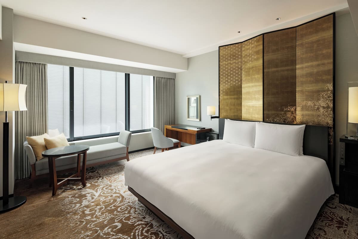 A hotel room with a large bed, a desk, a chair, and a sofa.