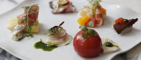 A white plate with various food items, including a red tomato, some fish, and garnishes.