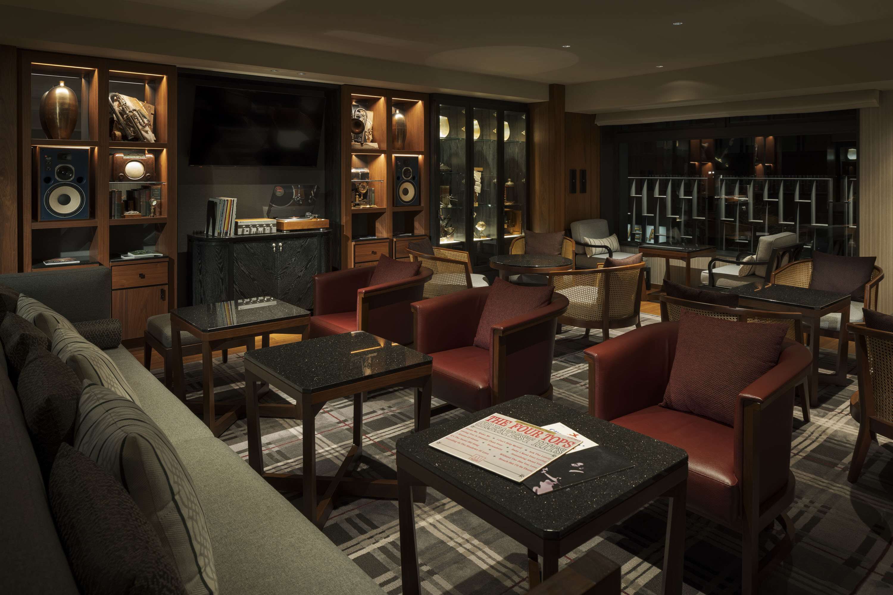 A modern hotel lobby with a sofa, armchairs, a coffee table, and a bookshelf.