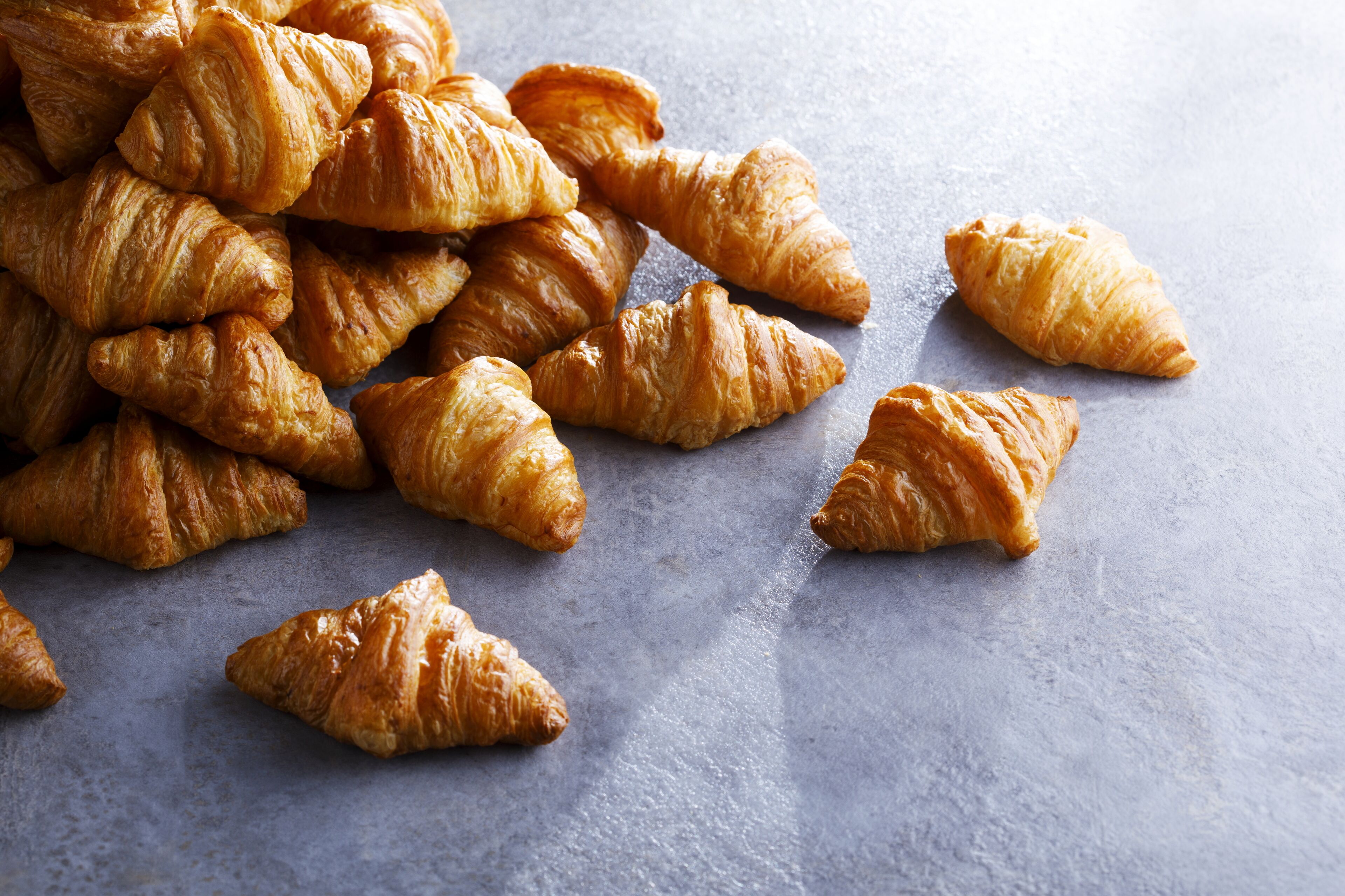 A pile of golden-brown croissants on a textured surface.