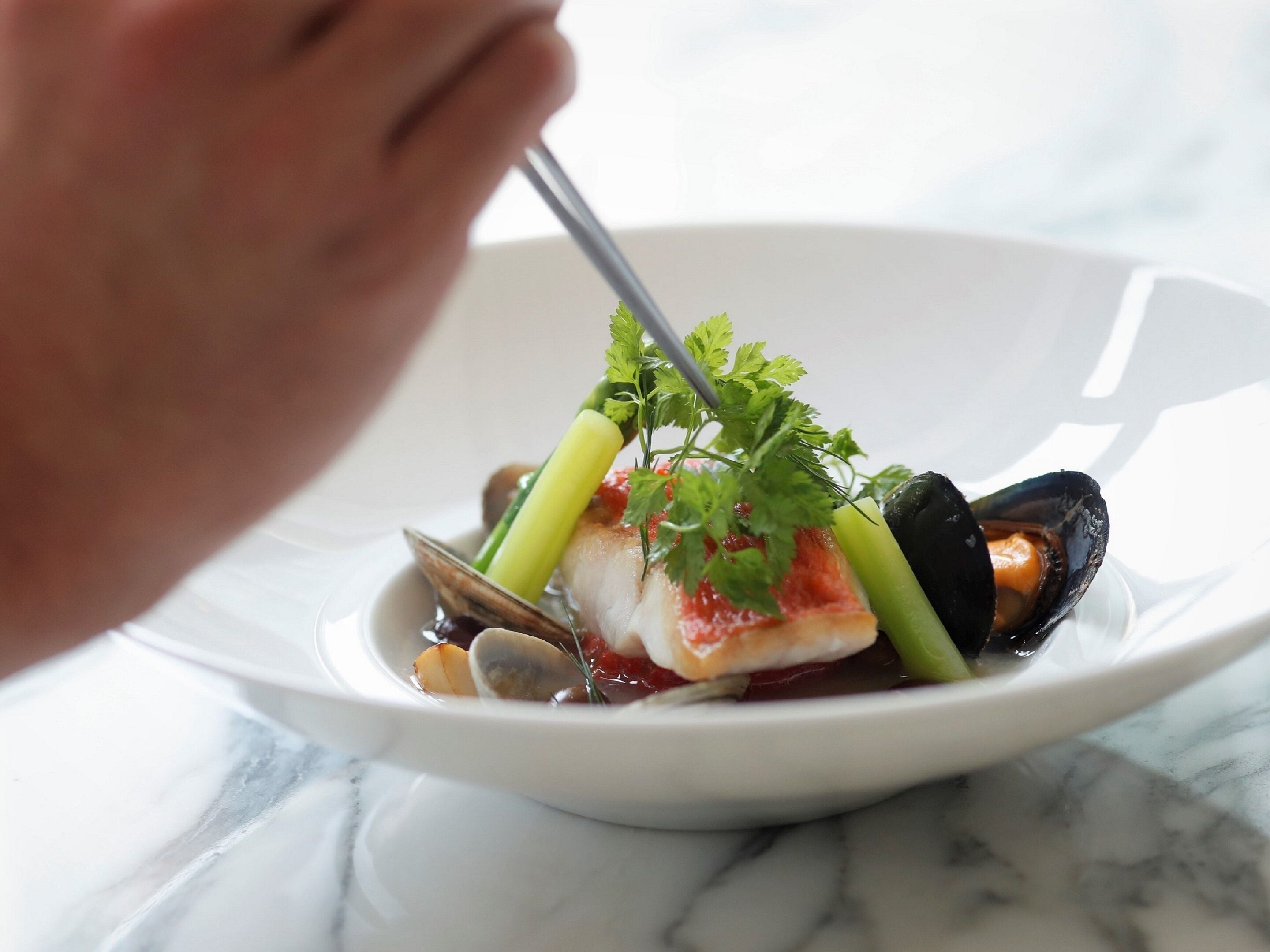 A white plate with seafood, including mussels and a fish fillet, garnished with herbs.