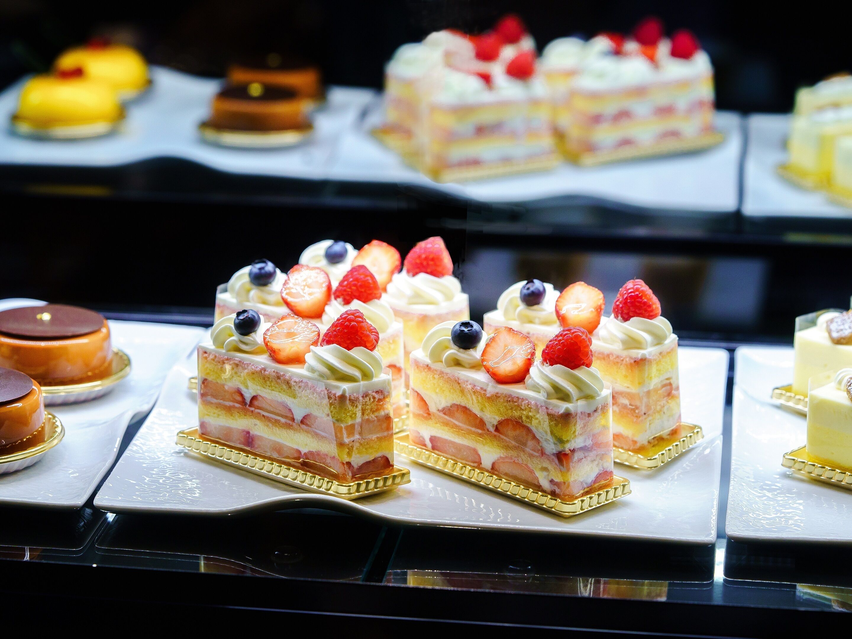 Una presentación de diversos postres, entre ellos pasteles en capas y productos de pastelería, sobre una superficie reflectante.