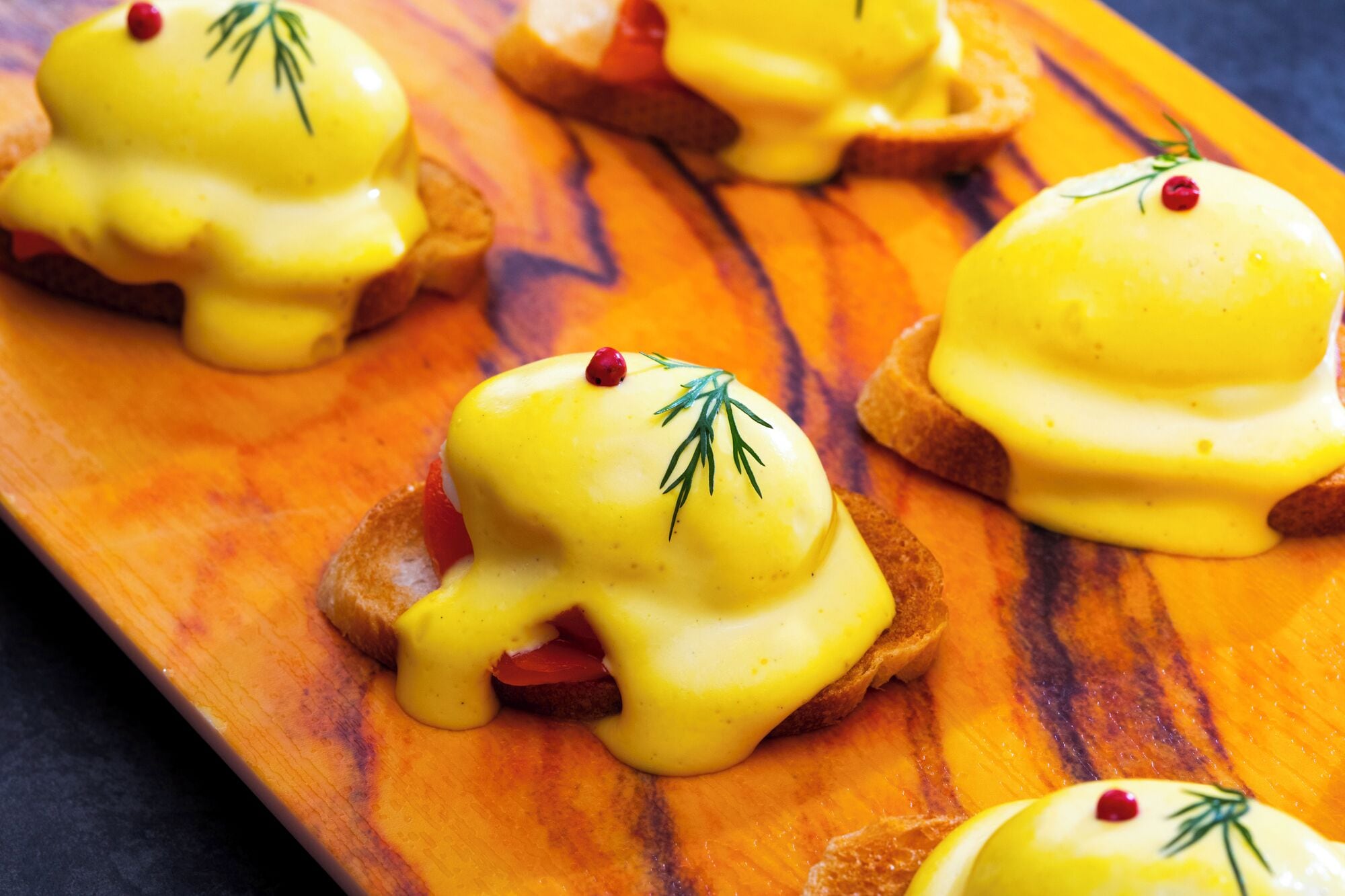 Una tabla de madera con varios sándwiches huevos benedictinos.